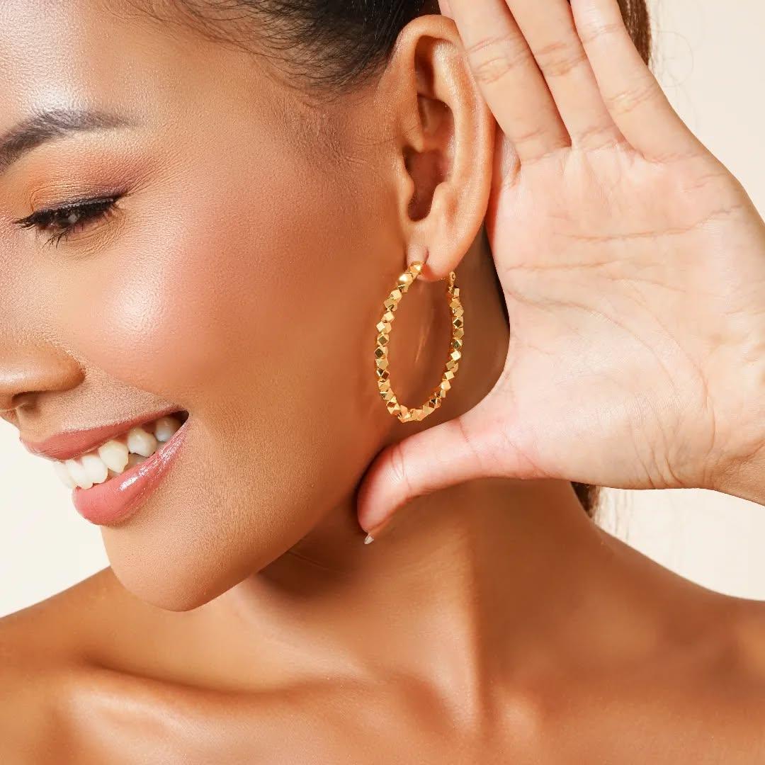 Smiling woman wearing textured gold hoop earring, close-up, modern jewellery style