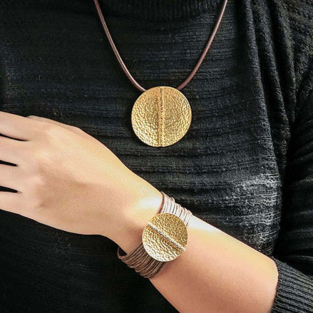 golden coin cord bracelet with large textured gold-tone coin on brown cord worn on wrist and neck