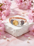 Verona Bracelet with four-tone gold, white, rose gold, and dark grey discs on elastic band surrounded by pink cherry blossoms and pearls