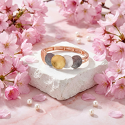 Verona Bracelet with four-tone gold, white, rose gold, and dark grey discs on elastic band surrounded by pink cherry blossoms and pearls
